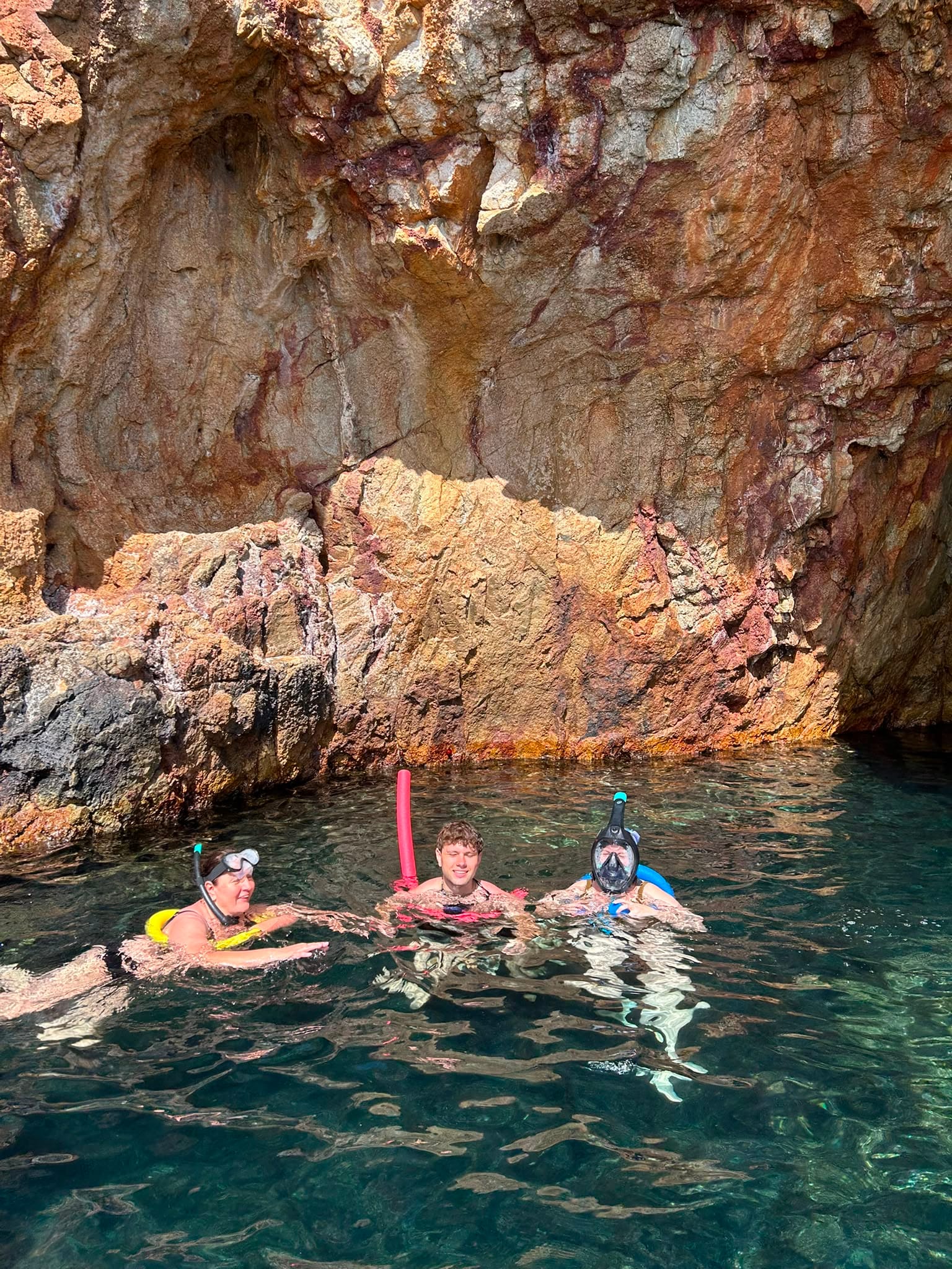 Guests snorkelling at the foot of an orange rock wall inside the grotto